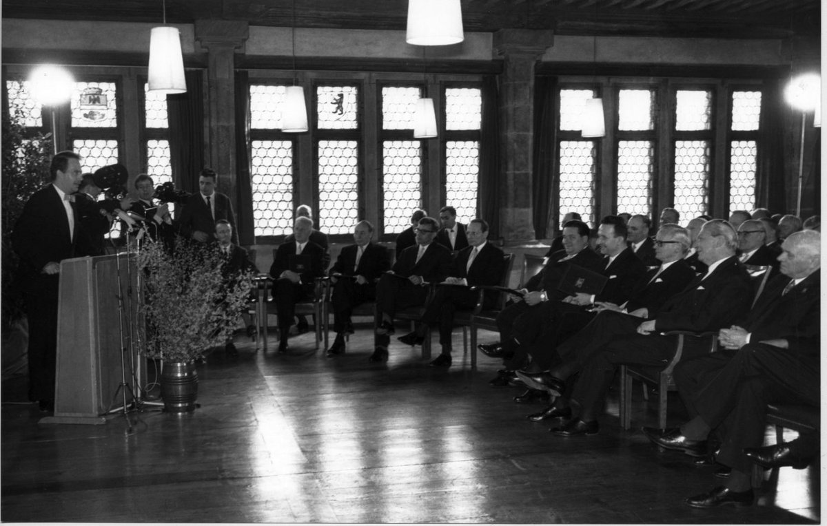 Kurt Georg Kiesinger stands at the lectern in the Rosengarten Museum. Various people sit in several rows of chairs in front of him.